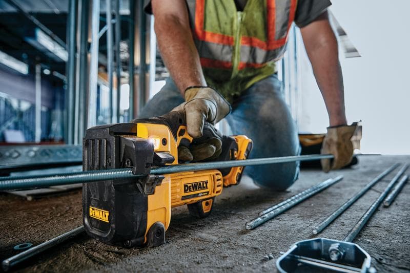 Uma pessoa usando luvas de trabalho e colete de segurança utiliza uma ferramenta de corte sem fio DEWALT para cortar uma barra de metal em um canteiro de obras.