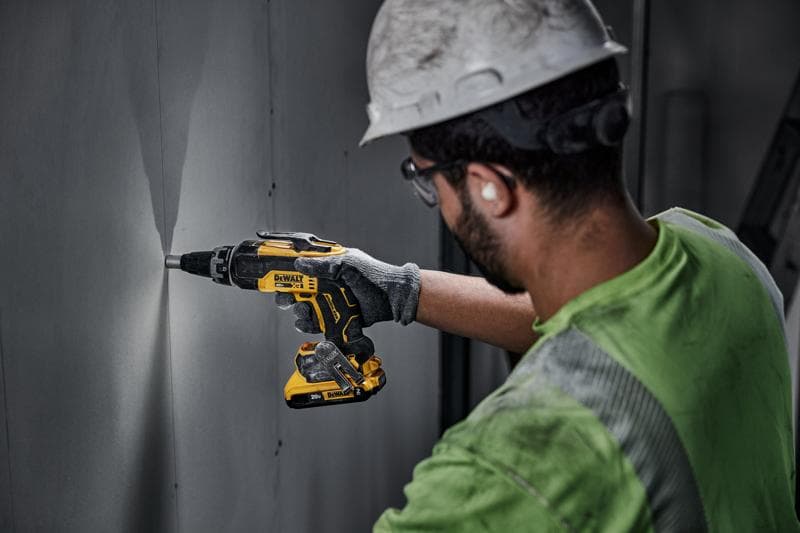 Uma pessoa usando capacete e luvas utiliza uma parafusadeira sem fio DEWALT DCF630D2 para trabalhar em um painel de parede em ambiente interno.