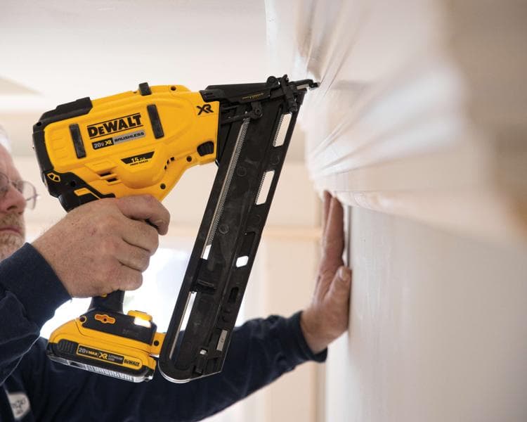 Uma pessoa usando uma pistola de pregos sem fio DEWALT 20V XR brushless para prender uma moldura na parede.