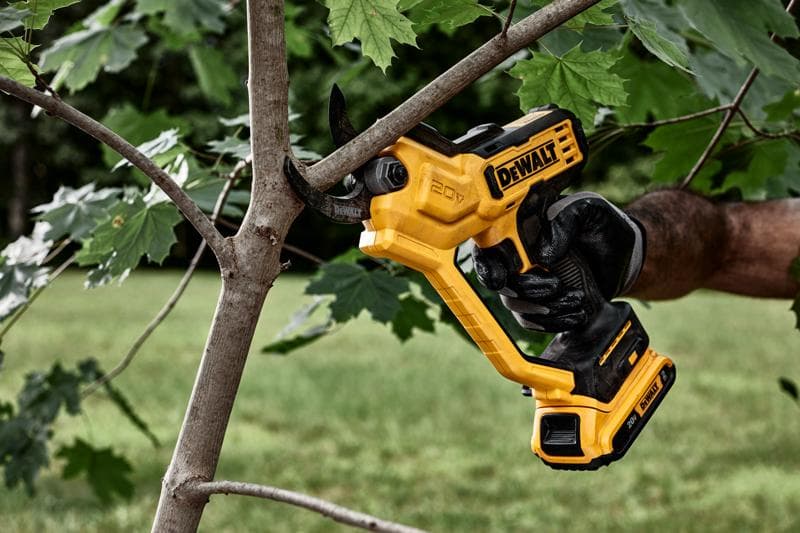 Uma pessoa usando uma luva preta está utilizando uma podadora elétrica sem fio DEWALT de 20V amarela para cortar um galho de uma árvore ao ar livre.