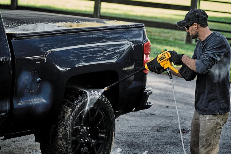 Uma pessoa está usando uma lavadora de alta pressão sem fio DEWALT DCPW550B para limpar a roda e a lateral de uma caminhonete preta ao ar livre.