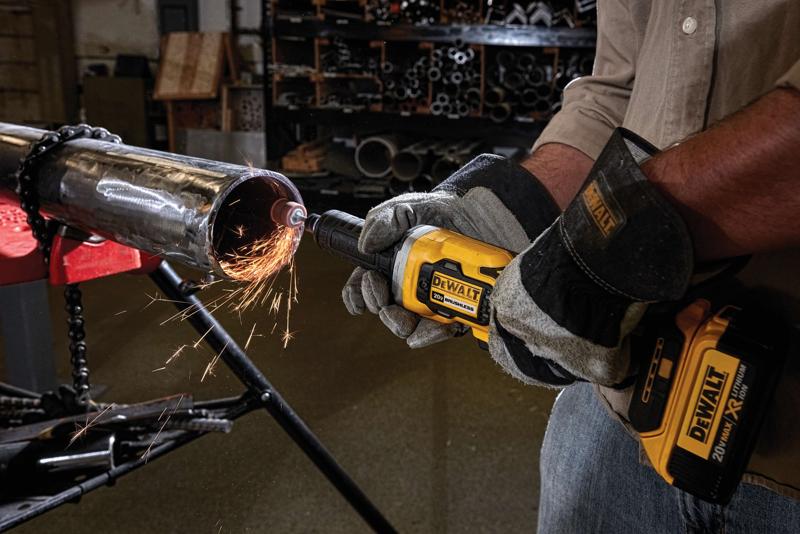 Uma pessoa usando luvas de proteção está utilizando uma esmerilhadeira sem fio amarela DEWALT para lixar a borda de um tubo metálico, produzindo faíscas em um ambiente de oficina.