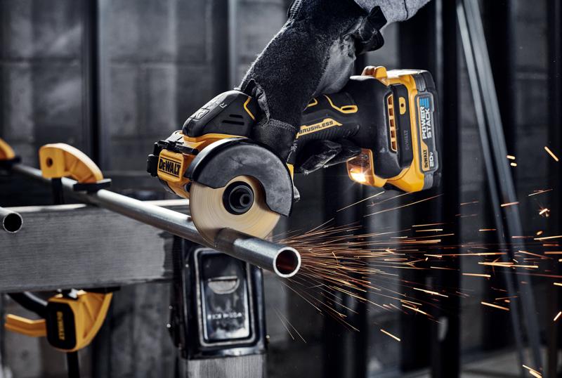 Uma pessoa com luvas usa uma esmerilhadeira angular sem fio brushless DEWALT para cortar um tubo de metal, produzindo faíscas em um ambiente de oficina industrial.