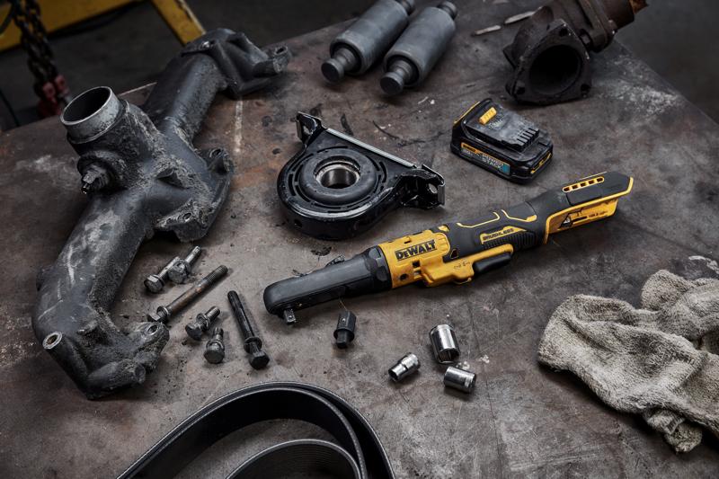 Ferramenta de catraca sem fio DEWALT DCF510B colocada em uma bancada de trabalho, cercada por várias peças automotivas, parafusos, soquetes, pacote de bateria e um pano sujo, sugerindo um ambiente de mecânica ou reparo.