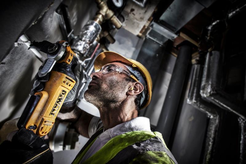 Trabalhador usa DEWALT DWE315 para cortar tubo, com capacete e colete em ambiente industrial.